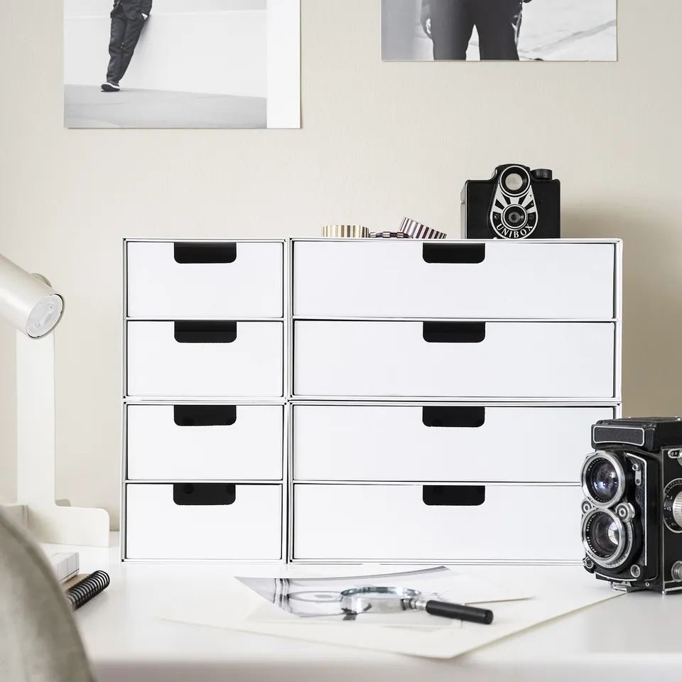 White FJÄDERHARV mini chest with black handles, eight drawers organising papers & photos, two vintage cameras on top.