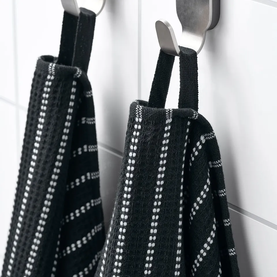 Two black waffle-textured towels with white patterns hang on hooks in bathroom.