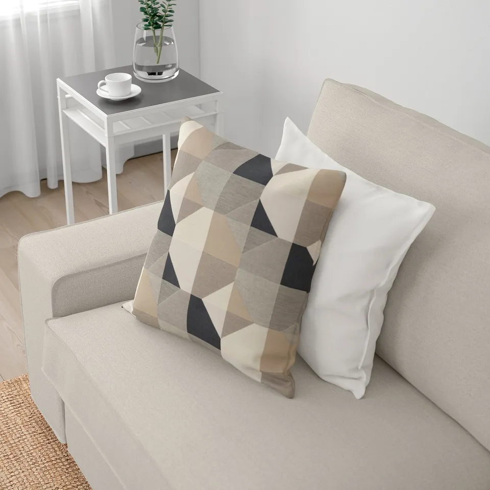 A modern living room with a KIVIK sofa, adorned with stylish pillows and an end table holding a teacup and plant.