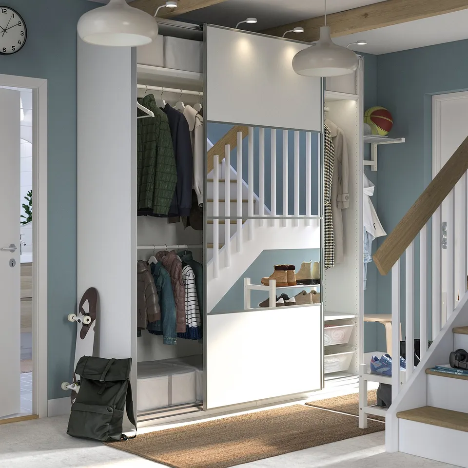 Depicts a modern, blue and white PAX wardrobe with mirrored sliding doors, housing clothes and accessories.