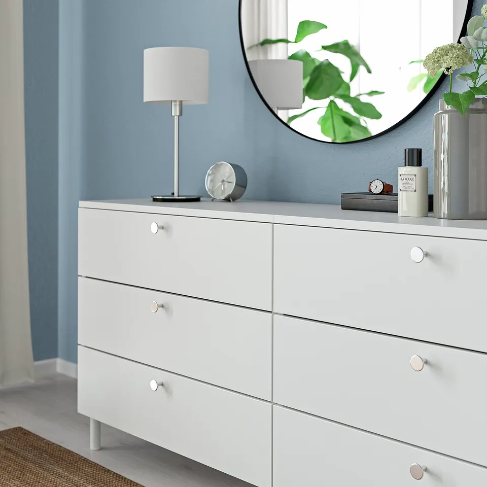 White dresser with modern knobs and a lamp on top.
