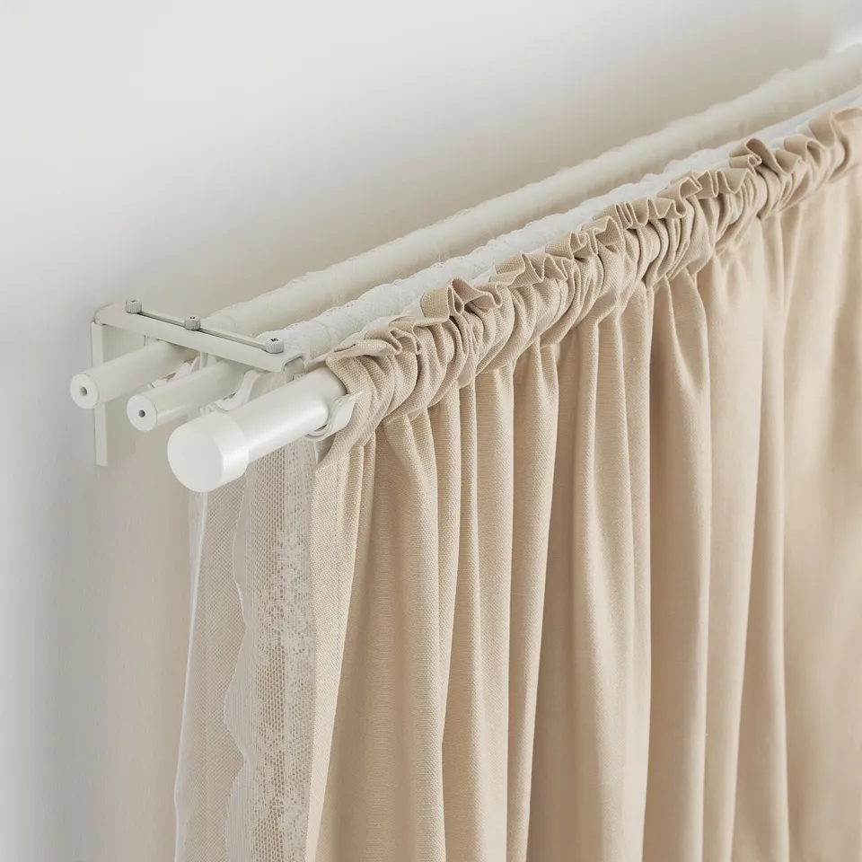 Image shows adjustable RÄCKA curtain rod in white metal holding beige curtains.