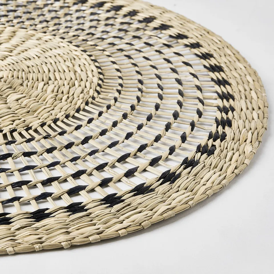 Handwoven round place mat, featuring intricate black and natural sedge patterns, offering a rustic yet elegant dining experience.