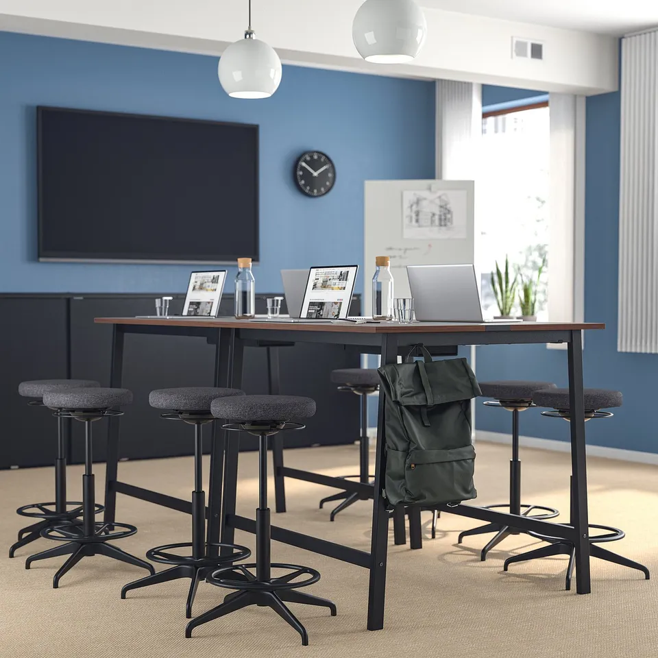 MITTZON conference table with dark wood top & black metal base, four adjustable stools, modern design, blue walls, tv, plants, lamps.