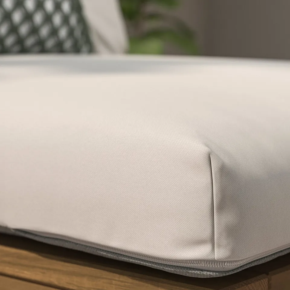 A close-up of a smooth, light grey outdoor cushion on wooden furniture, showcasing its fabric texture and stitching detail.