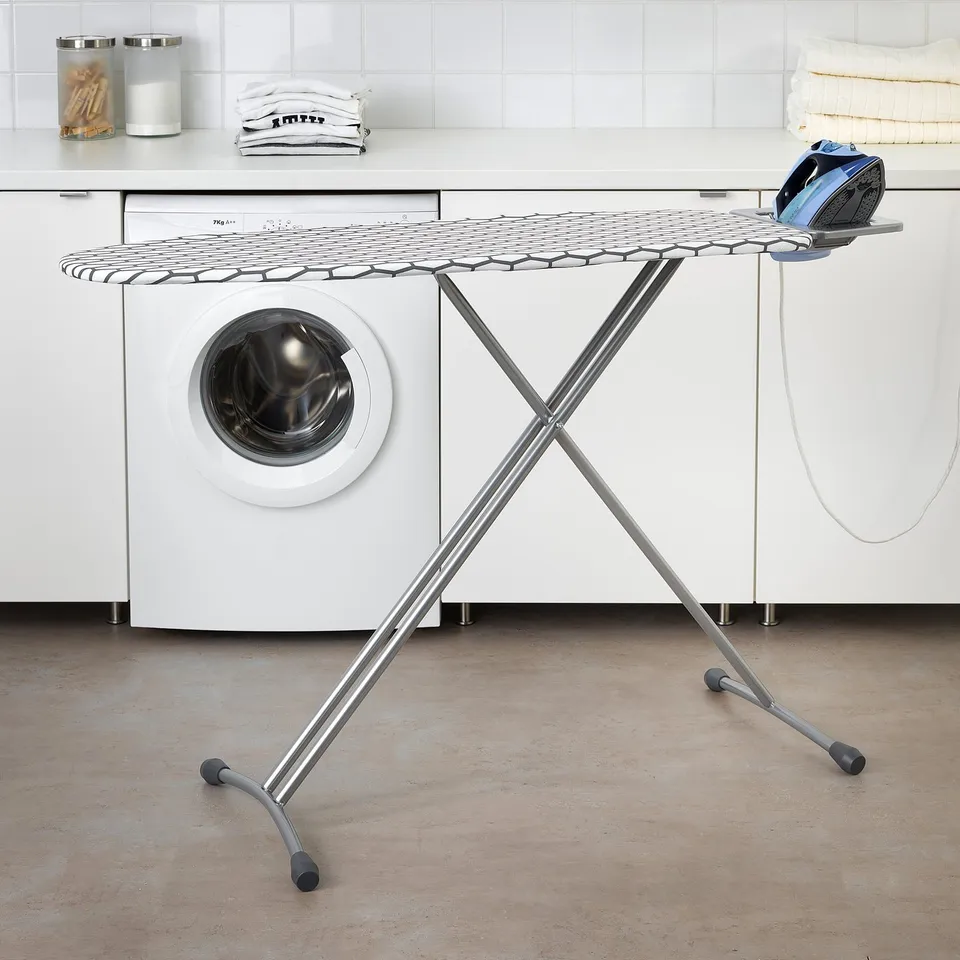 A white DÄNKA ironing board in laundry room with iron, beside washing machine and towels.