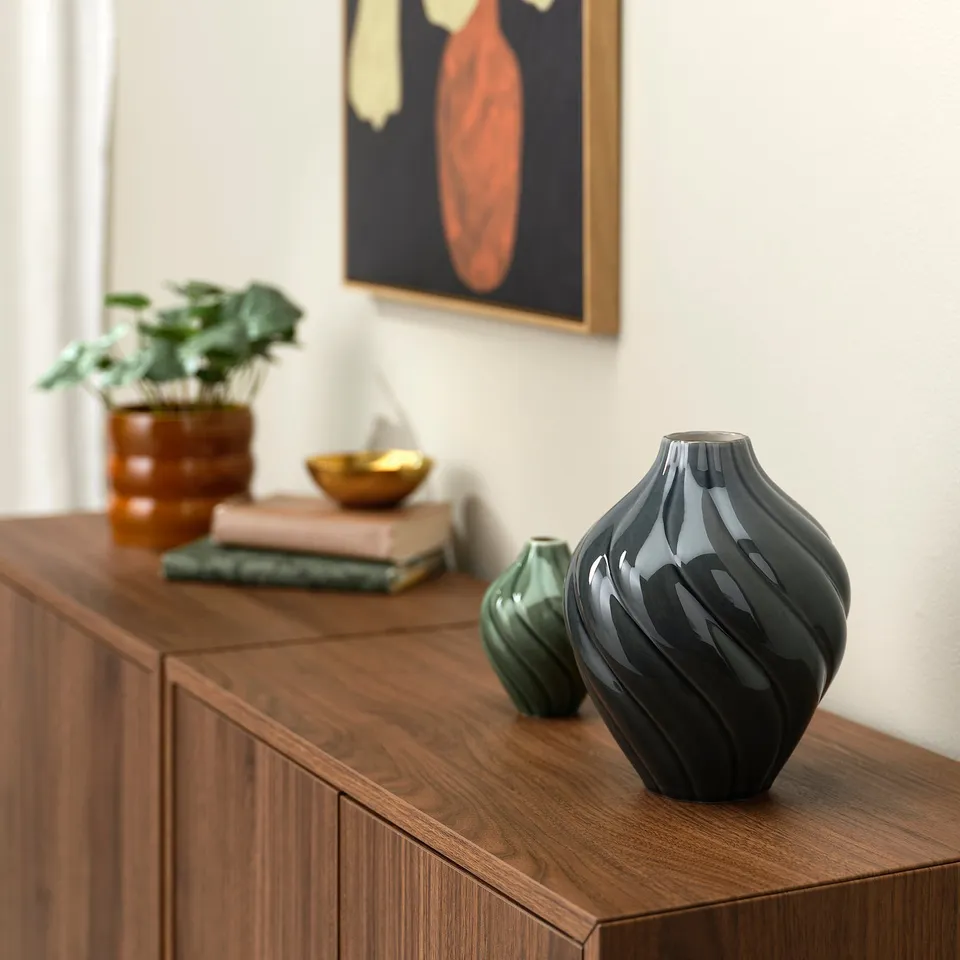 Wooden cabinet with KORNSPARV vases: black & green, unique glaze, smaller one in front, plant & decor behind.