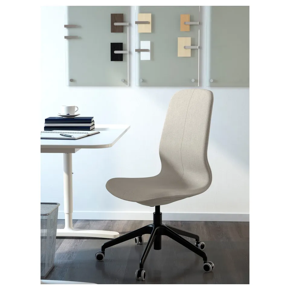Adjustable chair with lumbar support, books, cup on white table against glass wall with colours.