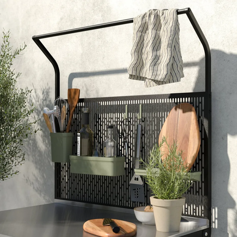 Black GRILLSKÄR outdoor kitchen organiser with hooks, containers, and rail. Holds utensils, cutting board, towel, and plants. Grey wall background.