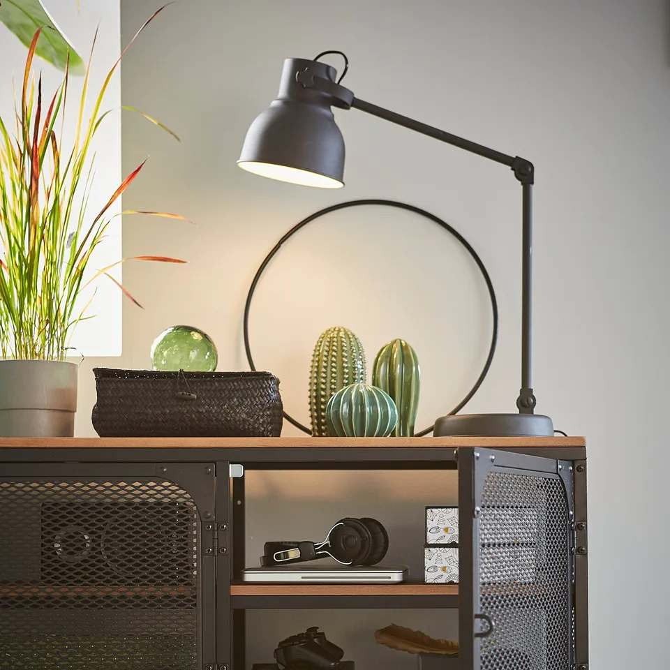 Industrial-style black metal and wood tv stand with various decor items on top, including a lamp, plants, and vases.
