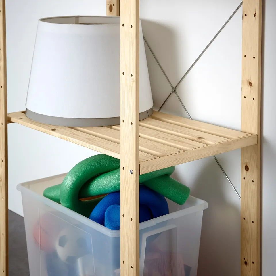 Wooden storage shelves holding a lamp and container with pool noodles. Sturdy design for home organisation.