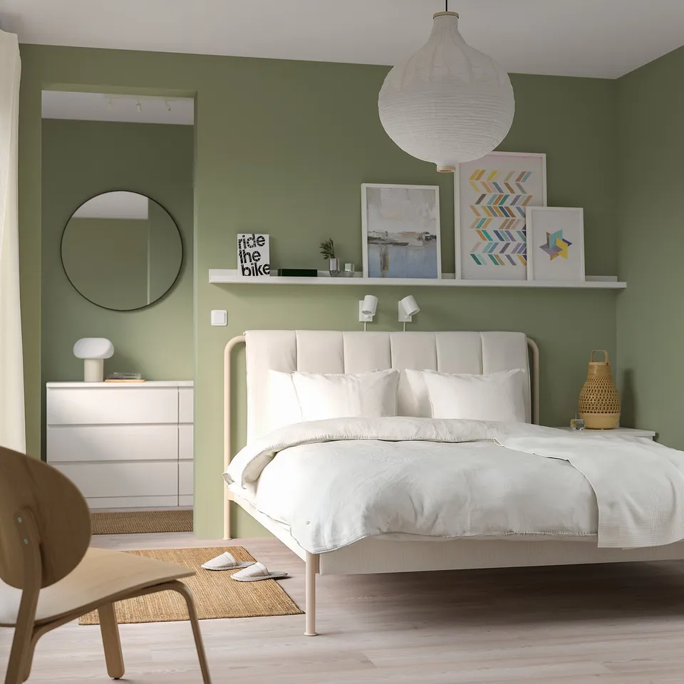 Modern bedroom with a TÄLLÅSEN bed, soft green walls, art, and jute rug.
