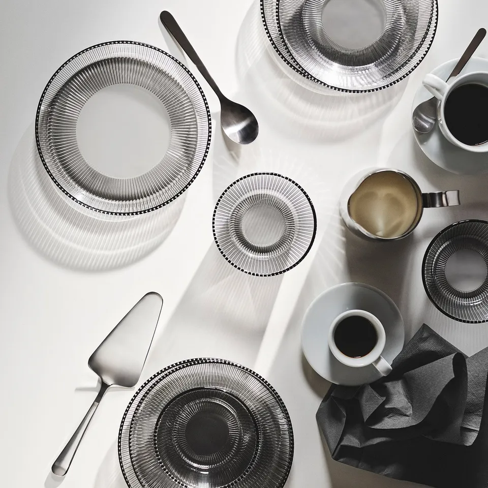 HAVSGÄDDA dinner set: grey, circular glass plates and bowls, stacked neatly, with sleek metal serving utensils.