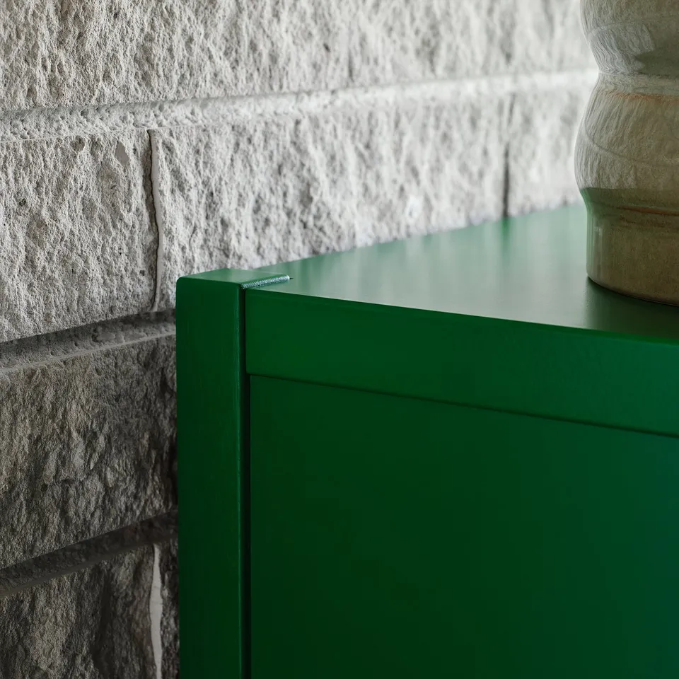 Green cabinet, white wall, vase, smooth surface.