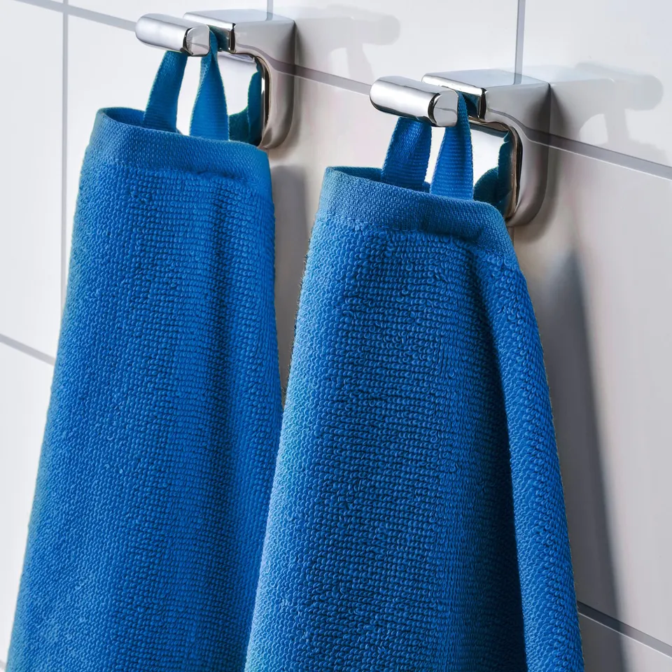 Two blue towels hang neatly side-by-side on chrome hooks against a white tiled wall.