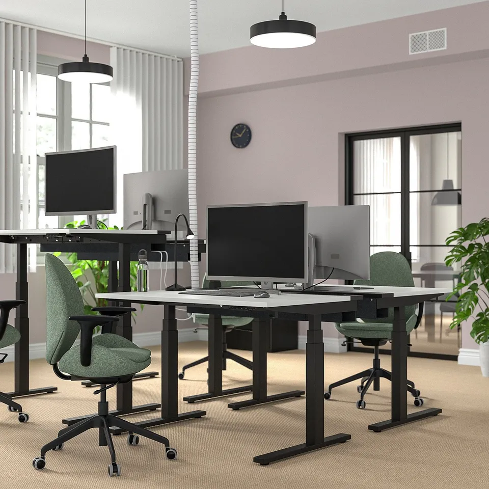 Modern office setup with MITTZON desks. Black desks with green chairs, computers, and plants. Spacious and well-organized.