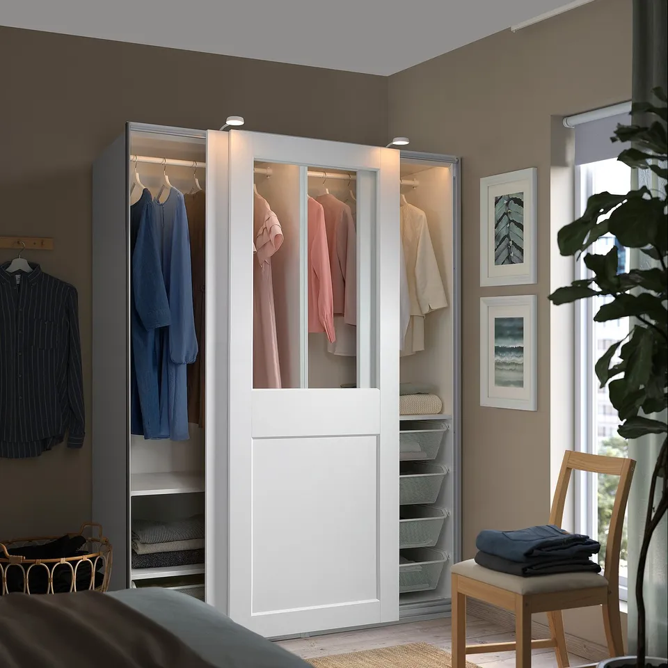 A large, white, modern PAX wardrobe with glass doors, neatly storing a variety of clothing items and accessories.