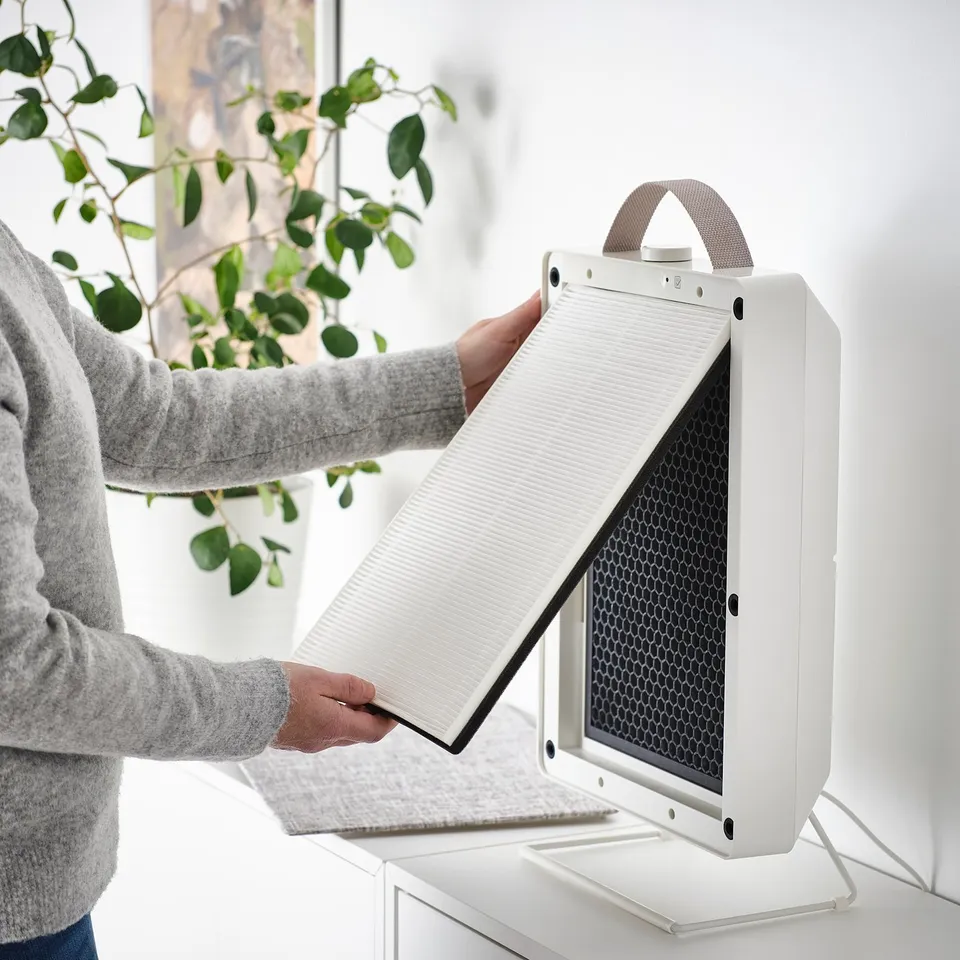 Person instals philtre into white air purifier. The philtre helps remove dust, pollen, and smoke.