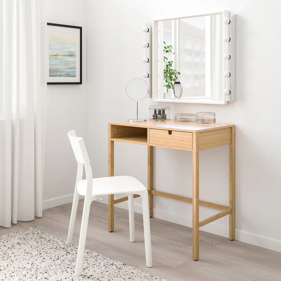 Modern minimalist vanity set: light wood desk, white chair, mirror with lights. Small, neat, well-lit setup.
