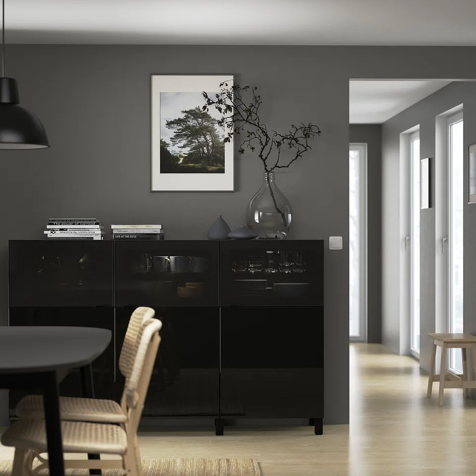 Modern dining area with black BESTÅ sideboard displaying dishware. A framed nature photo hangs above. Wooden chair visible in front.