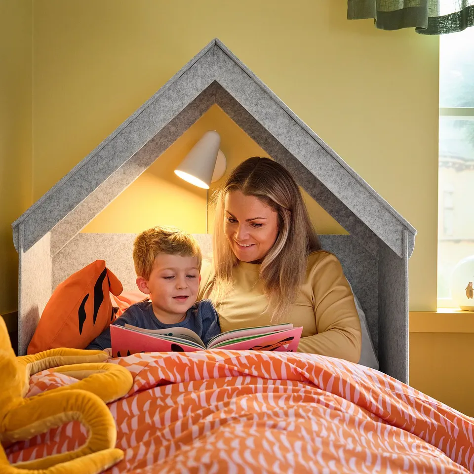 A person and a boy read together on a SLÄKT bed, illustrating its cosy nook.