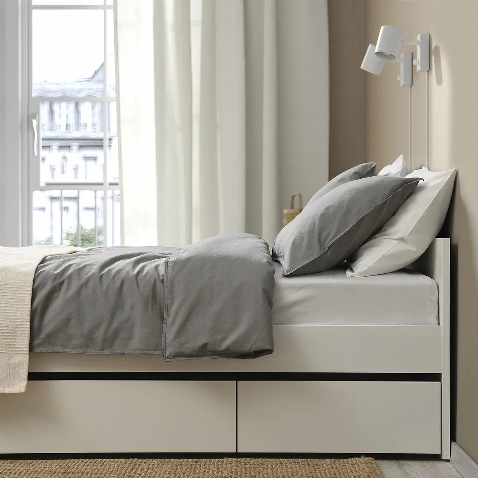 Modern bed frame with two drawers, near a window. Minimalist decor with light curtains.