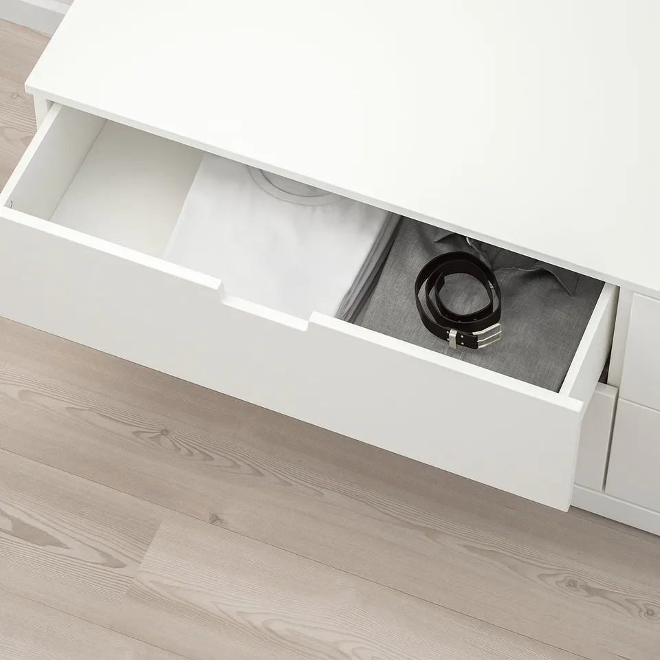 Open white NORDLI chest drawer revealing a belt and shirt on wooden floor.