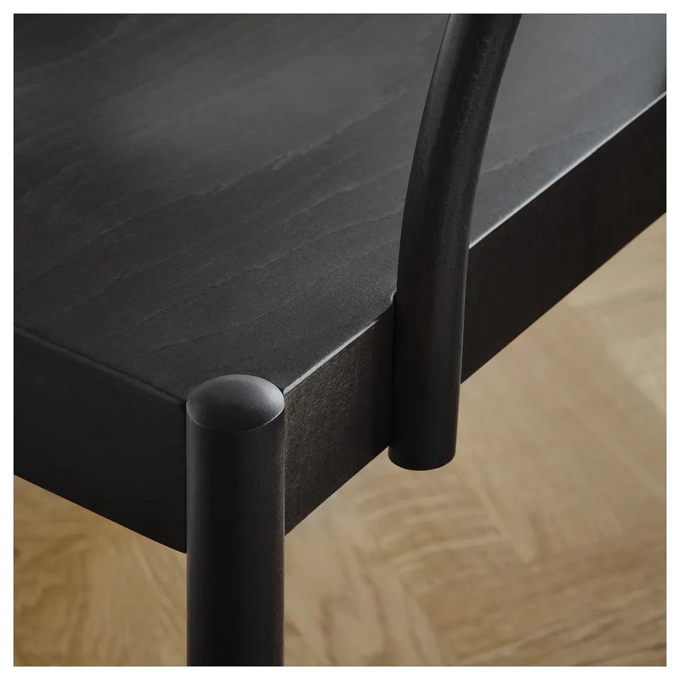 Modern chair close-up: sleek black metal legs, fine wooden seat edge detail, sturdy construction.