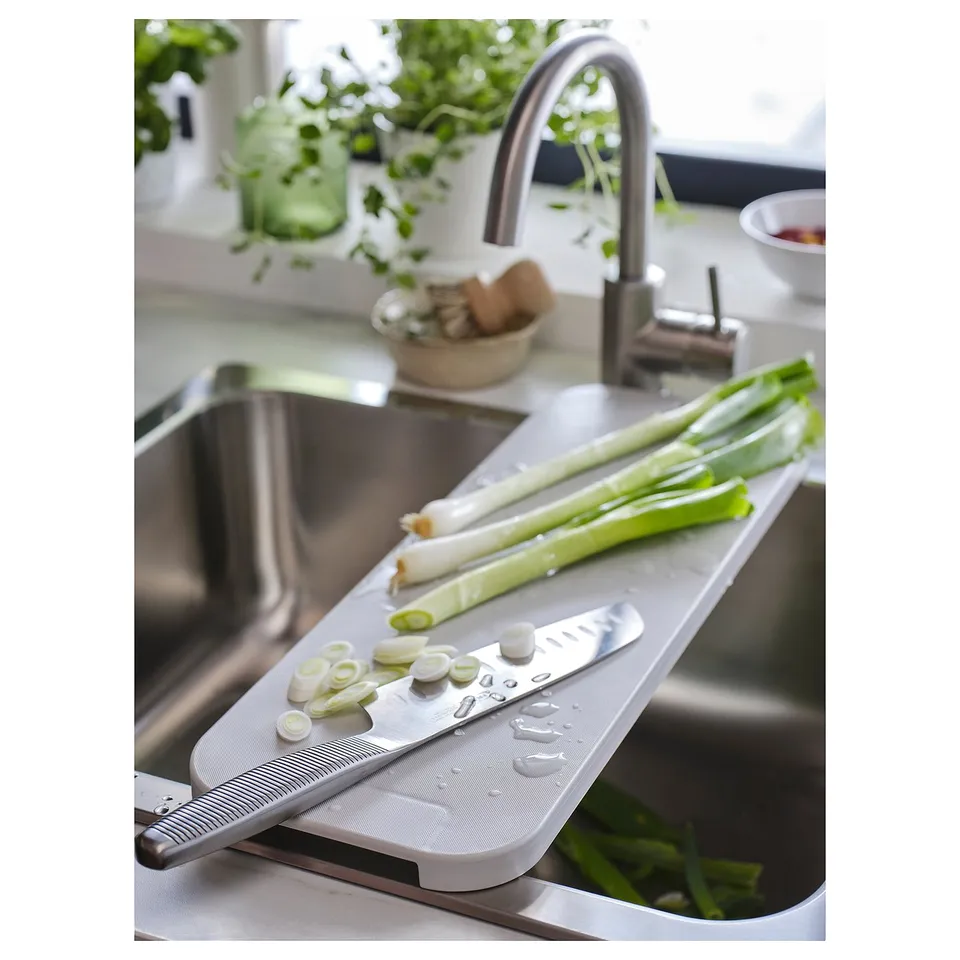 White chopping board over sink, green onions and sliced scallions, stainless sink, plants, kitchen setup.