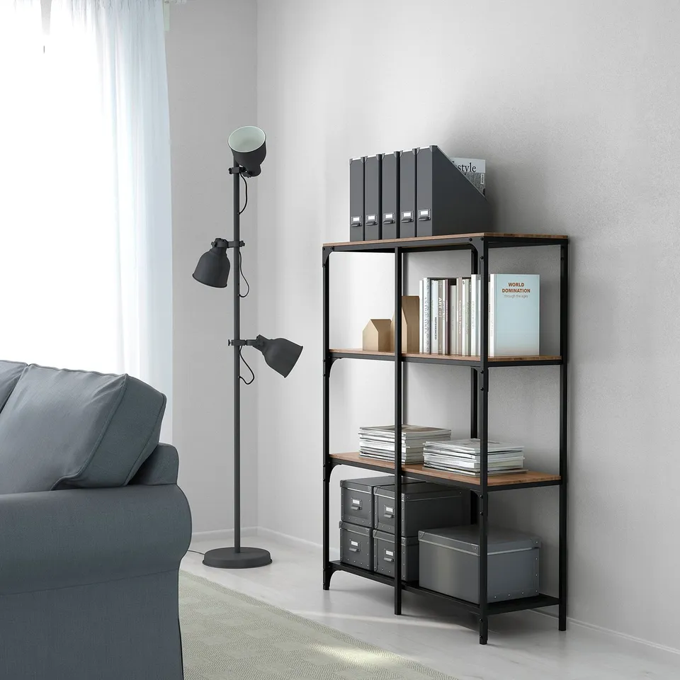 Modern metal and wood bookshelf holding books, binders, and storage bins in a tidy room with a stylish lamp.