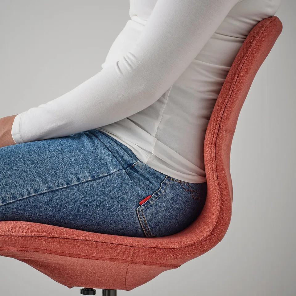 Person sitting on a pink office chair, wearing jeans and a white shirt. The chair lumbar support and a height-adjustable seat.