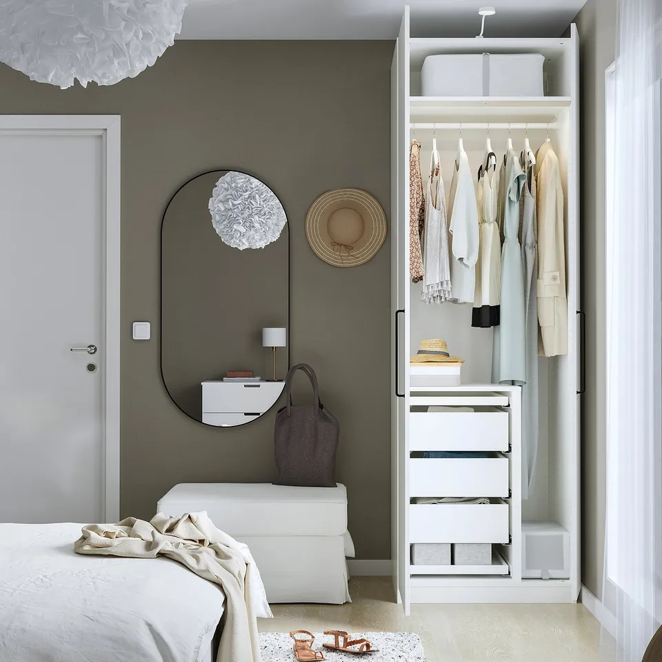 Minimalist bedroom with PAX wardrobe showing organised clothes, drawers, and hanging space. Mirror and decorative items enhance the rooms aesthetic.