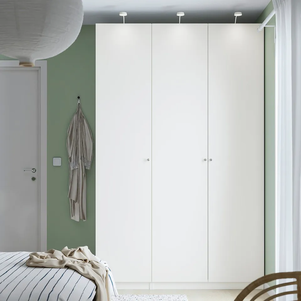 Modern room with PAX wardrobe, beige bed linens, and a hanging garment. Minimalist style with green walls.