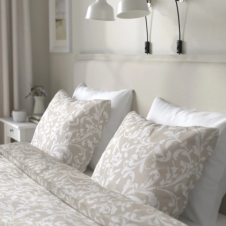 Bed with floral-patterned pillows, soft headboard, wall-mounted lamps, and bedside vase.