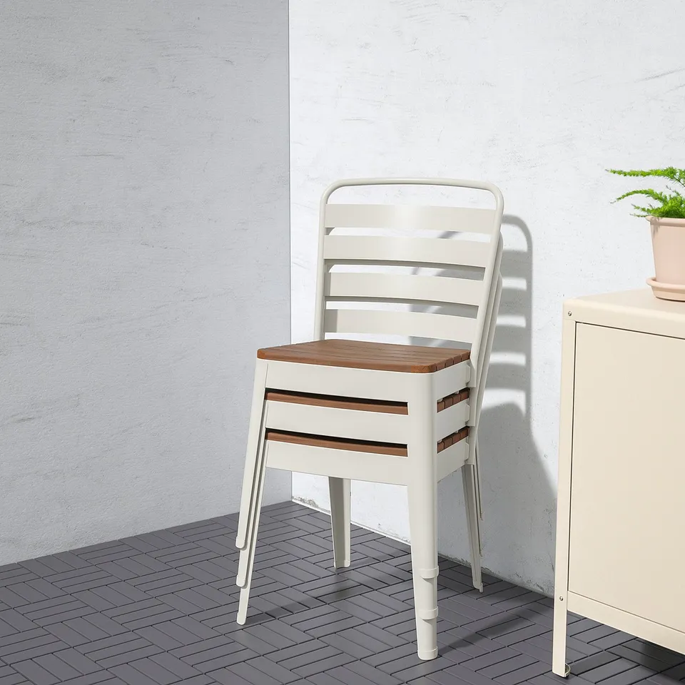 A white metal chair with wooden seat and back, placed against a light wall.