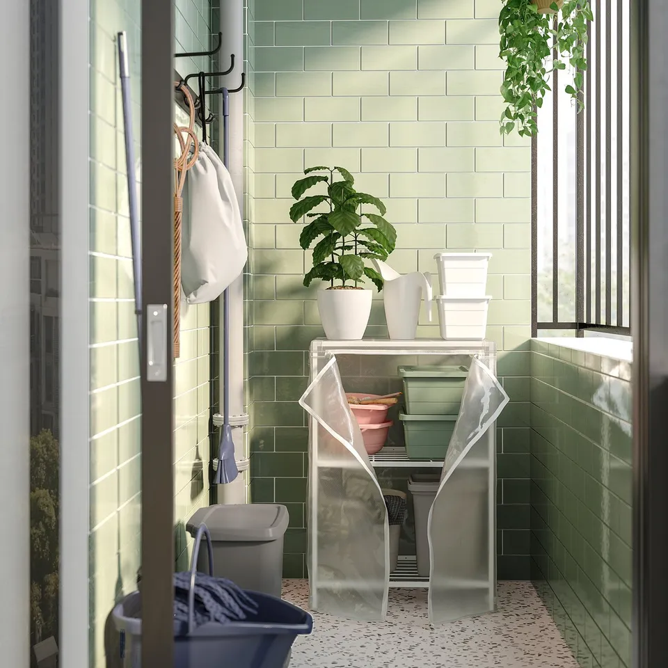 Slanted glass door revealing green-tiled balcony with white shelving, potted plants, and mesh storage containers.