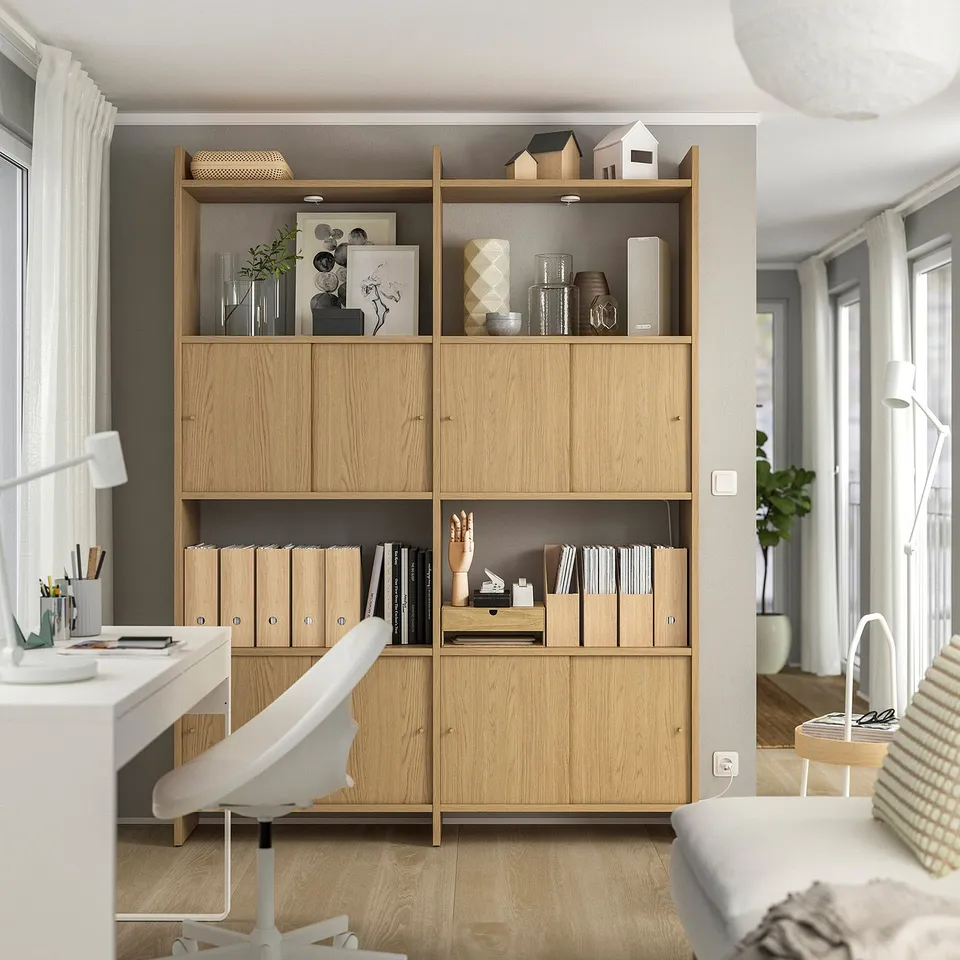 Modern wooden bookshelf, LÅDMAKARE, light wood, organised with books, decor, and office supplies, adjacent to a white desk and chair.