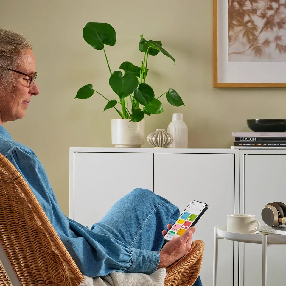 Person using smartphone with apps, plant, books, mug.
