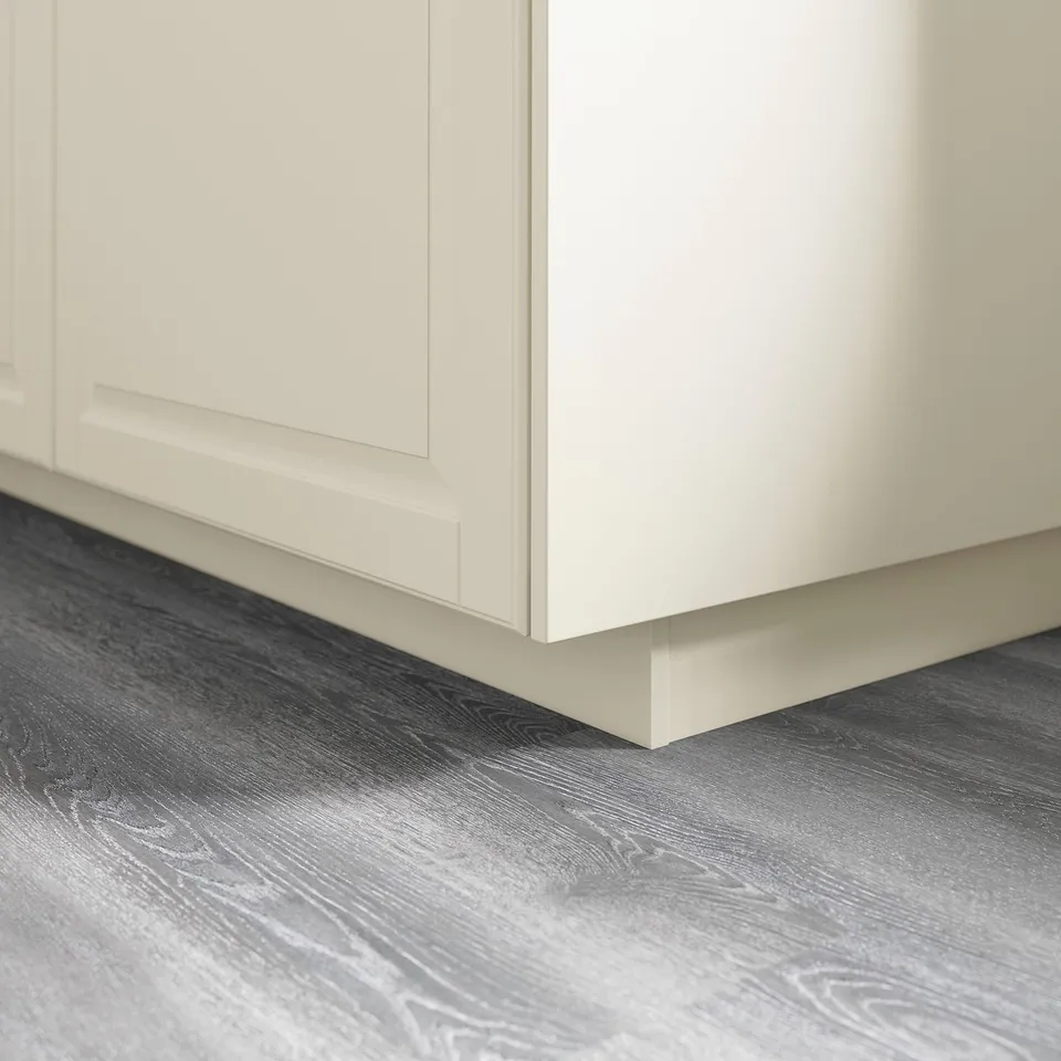 White kitchen cabinet plinth on grey wood floor.