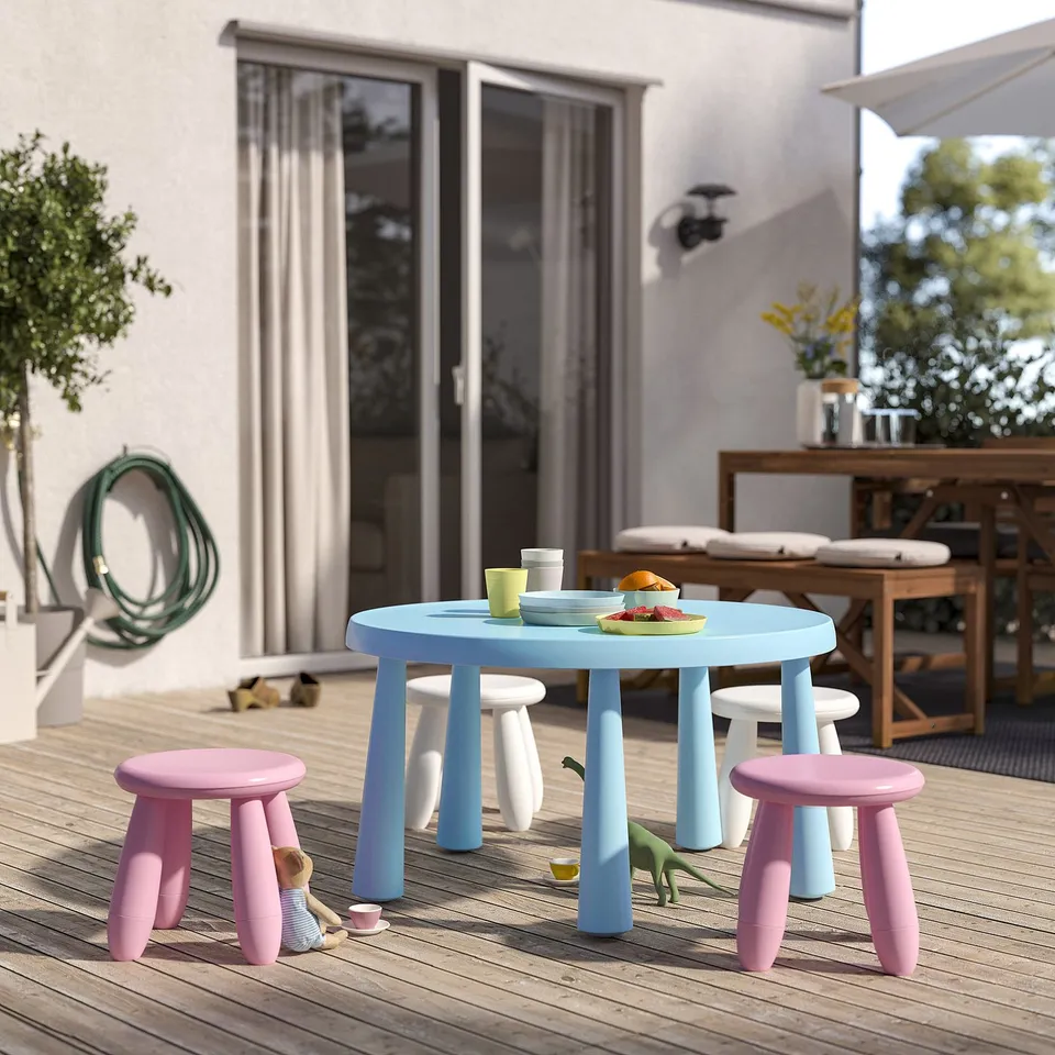 A blue MAMMUT childrens table and pink chairs with small toys on a wooden deck. The furniture is compact and colourful, designed for outdoor use.