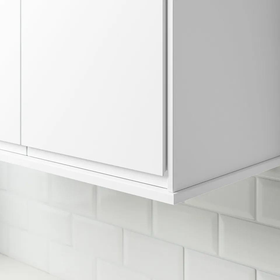 White cabinet trim installed under a kitchen cabinet, concealing lighting and cords, showcasing its functional design.