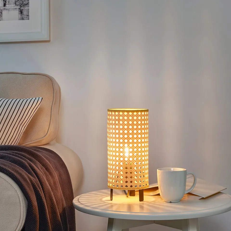 Bamboo-style lamp on table, casting shadows, next to chair and mug.