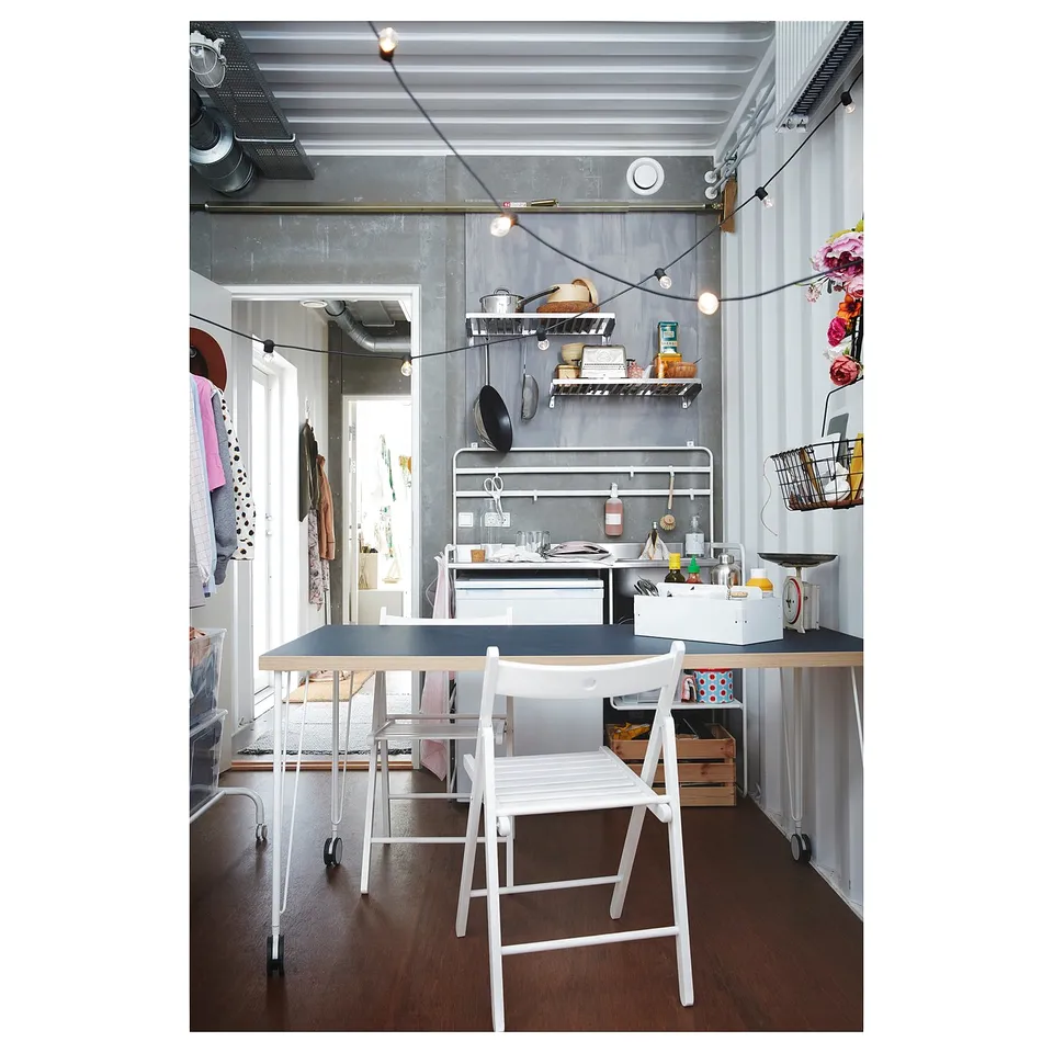 Small kitchen setup with white furniture, string lights, and wall-mounted shelves.