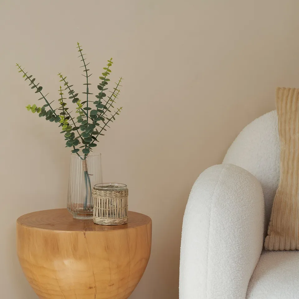 Clear vase with eucalyptus stems sits on round wooden table.