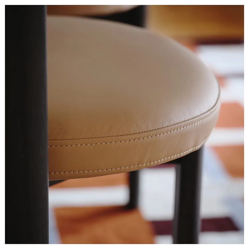 Close-up of a modern chair made with tan leather and black metal frame, showcasing high-quality stitching and design.