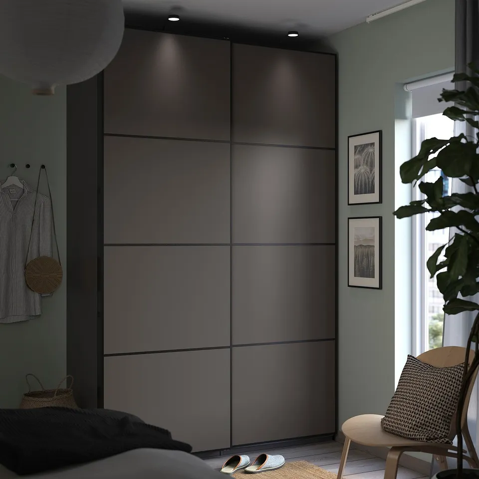 Modern bedroom featuring a dark grey PAX wardrobe with sliding doors, herbs green walls, minimalist decor, and wooden chair with a cushion.