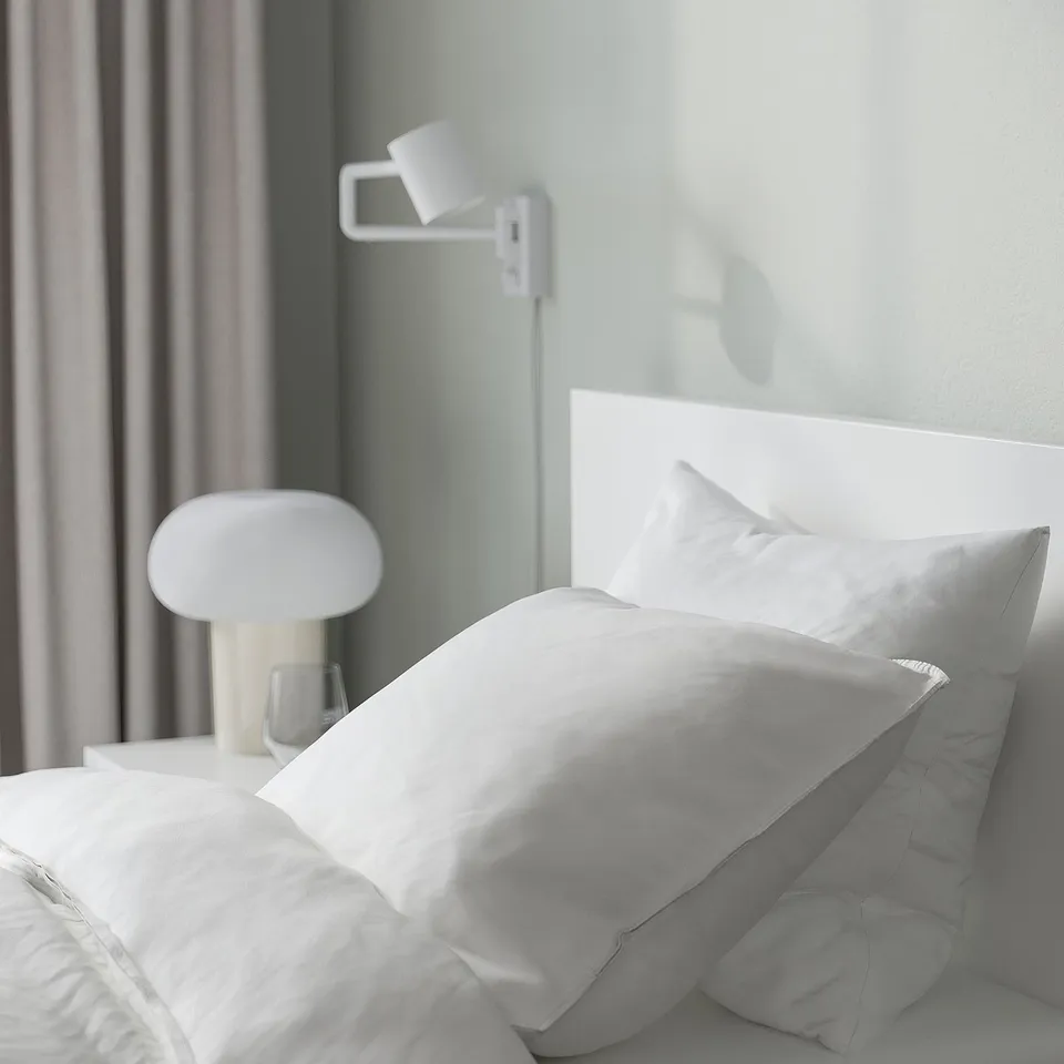 Minimalist bed with adjustable headboard, white lamp, and cosy pillows.