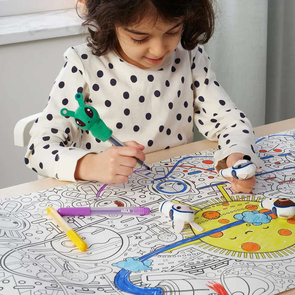 Child draws with markers on large space-themed colouring mat, using finger puppets.