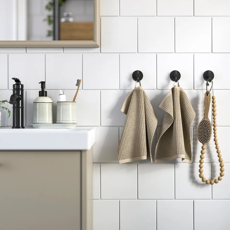 Modern bathroom with white tiled walls, black tap, soap dispensers, and beige GULLDYNA towels on hooks.