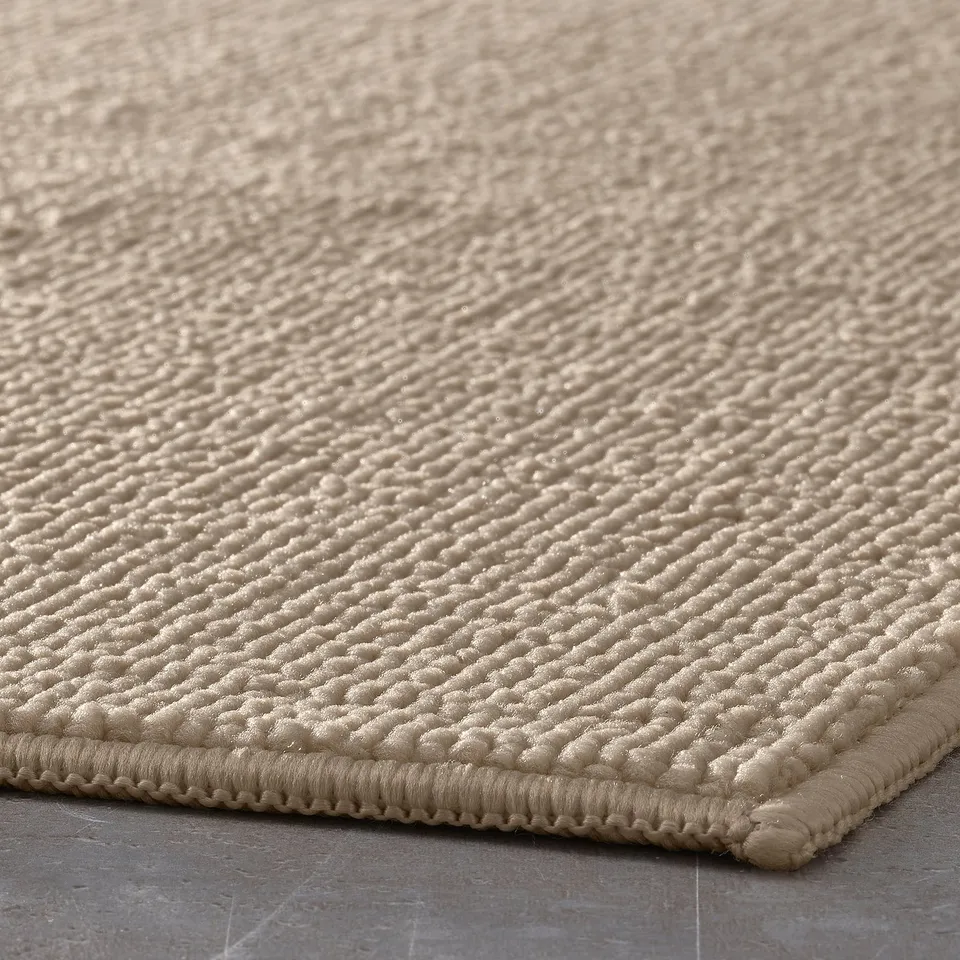 Beige FINTSEN bath mat displayed in close-up, showcasing its soft, textured surface and stitched edge.